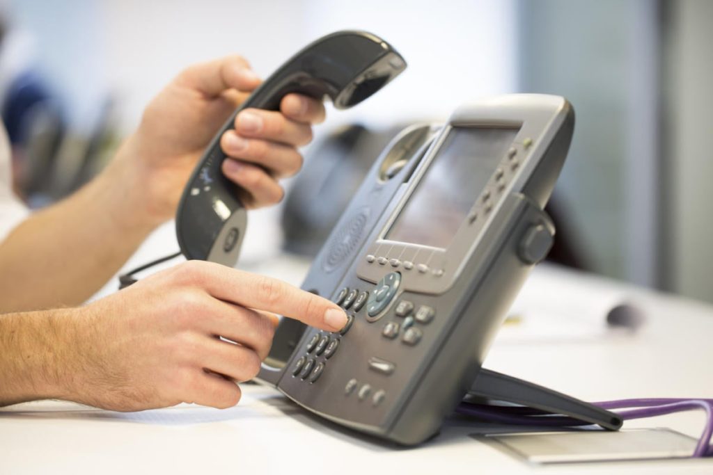 Hands dialing a Cisco IP desk phone in an office
